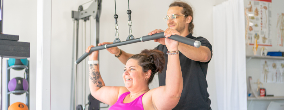 Fitness instructor teaching woman lat pulldowns inside gym